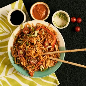 A vibrant bowl of noodles with fresh vegetables and accompanying sauces, perfect for food photography.