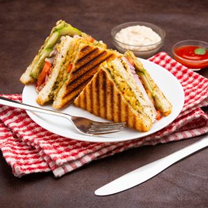 Grilled vegetable sandwich served on a white plate with sauces.